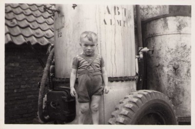Johan Snijders voor een machine van de ABTB Almelo dat aardappels kookt en verwerkt tot varkensvoer. Johan verteld dat hij deze machine machtig interessant vond omdat er veel stoom vanaf kwam. De foto is gemaakt bij de boerderij aan de Brinkstraat 25 Reutum. De Boerderij had als bijnaam Mös. Uit het fotoarchief van Johan Snijders.